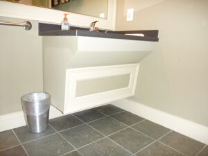 A sink with clearance underneath as well as a panel covering the plumbing pipes.