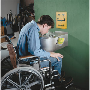 A person in a wheelchair using an accessible emergency eyewash station.