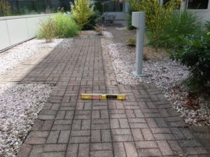 Exterior pathway of pavers with planting beds on either side. A 2 foot digital level is placed to measure cross slope.