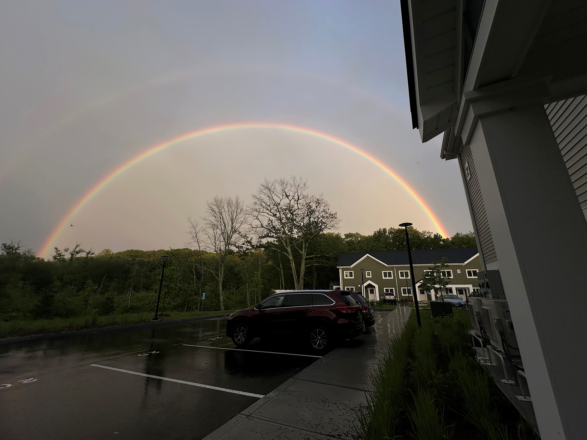 Double rainbow arching over Eagleville Green with vibrant colors above a row of townhouses and a wet parking lot, suggesting recent rainfall.
