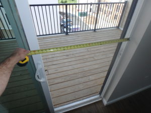 A sliding glass door at a balcony is opened fully with a measuring tape held across the clear opening. A dimension of 30.75 inches is shown, less than the required clear width.