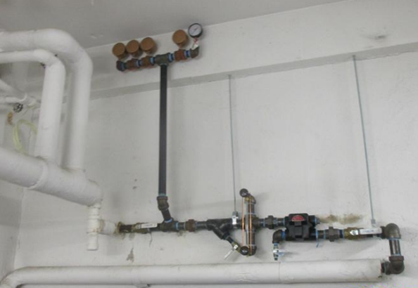Piping assembly on an interior wall showing multiple steam system components, including air vents mounted at the top of a vertical pipe and additional valves and fittings along the horizontal piping below.