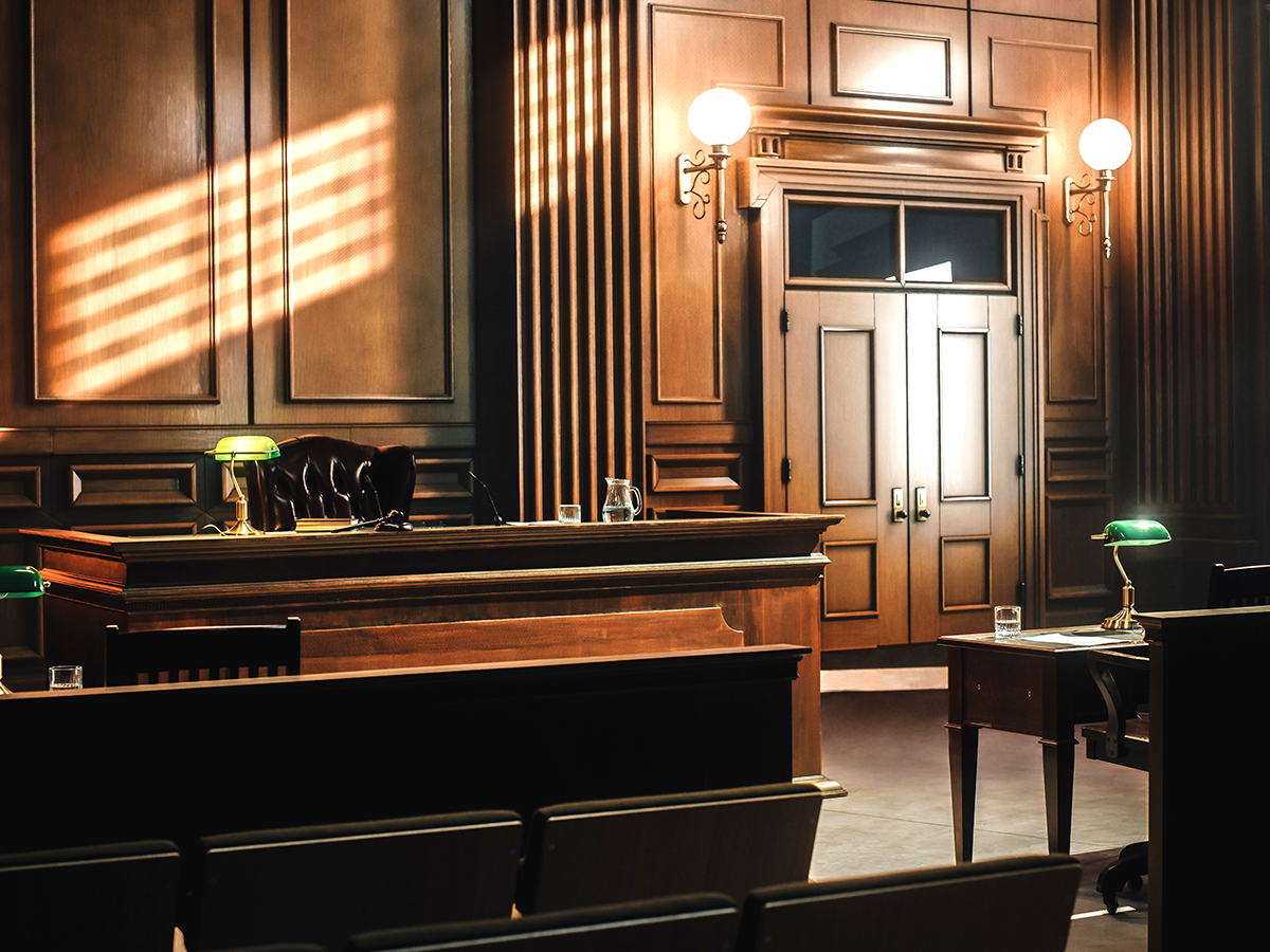 Empty courtroom interior with judge’s bench, counsel tables, and seating viewed from the gallery.