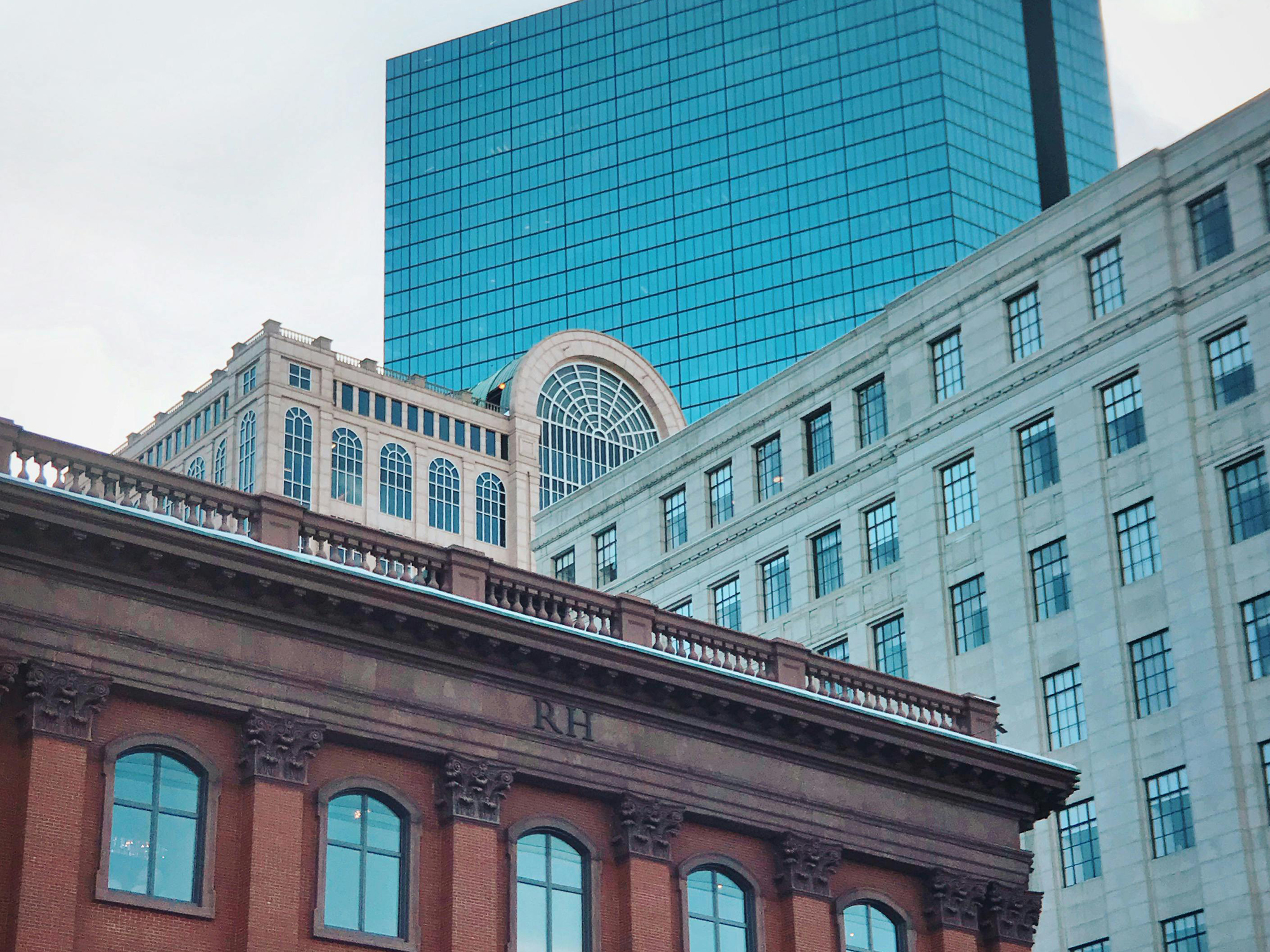 Boston buildings including a historic red brick building with arched windows, set against modern buildings with beige stone and blue glass exteriors, illustrating the city's blend of old and new architecture.