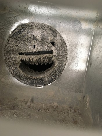 Constant airflow regulator inside a ventilation duct coated with dust and debris, restricting airflow and affecting ventilation system balance.