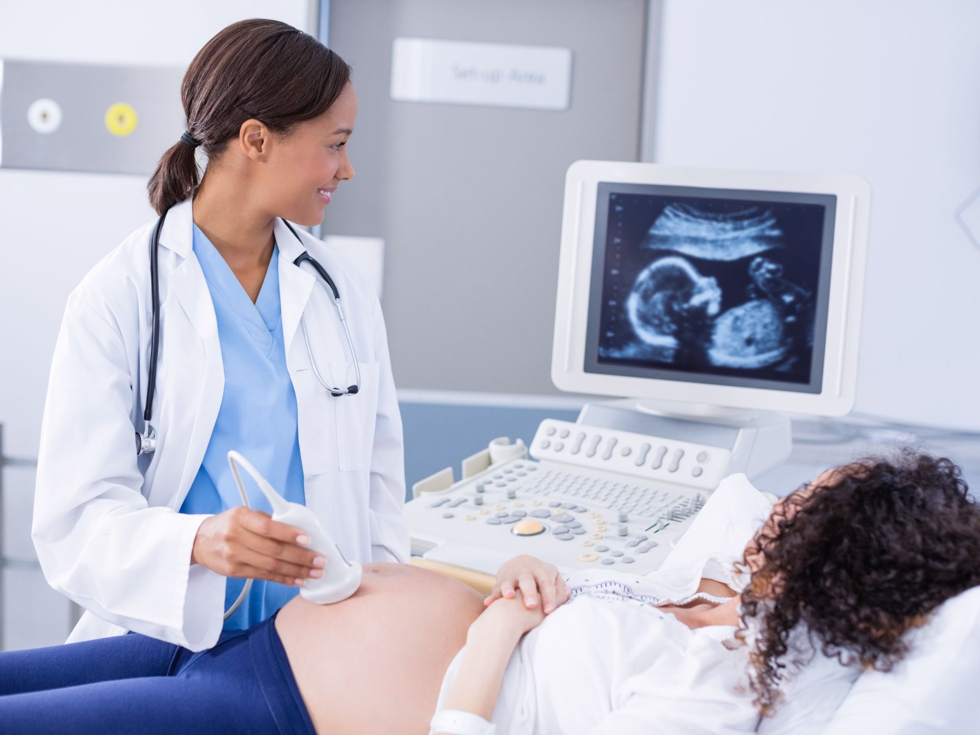 Healthcare provider conducting an ultrasound examination with fetal images visible on a monitor.