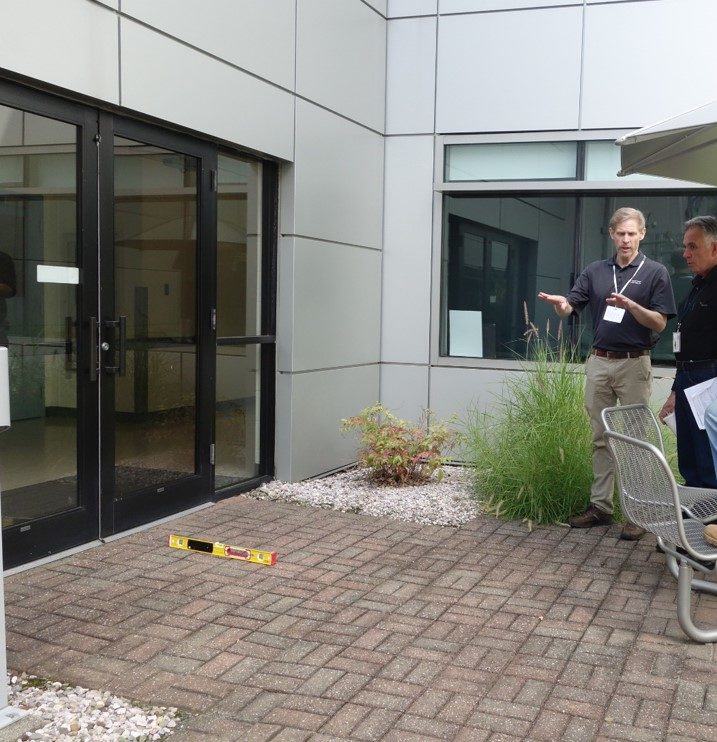 Pavers leading up to a building entry door with a 2 foot digital level measuring slope perpendicular to the door.