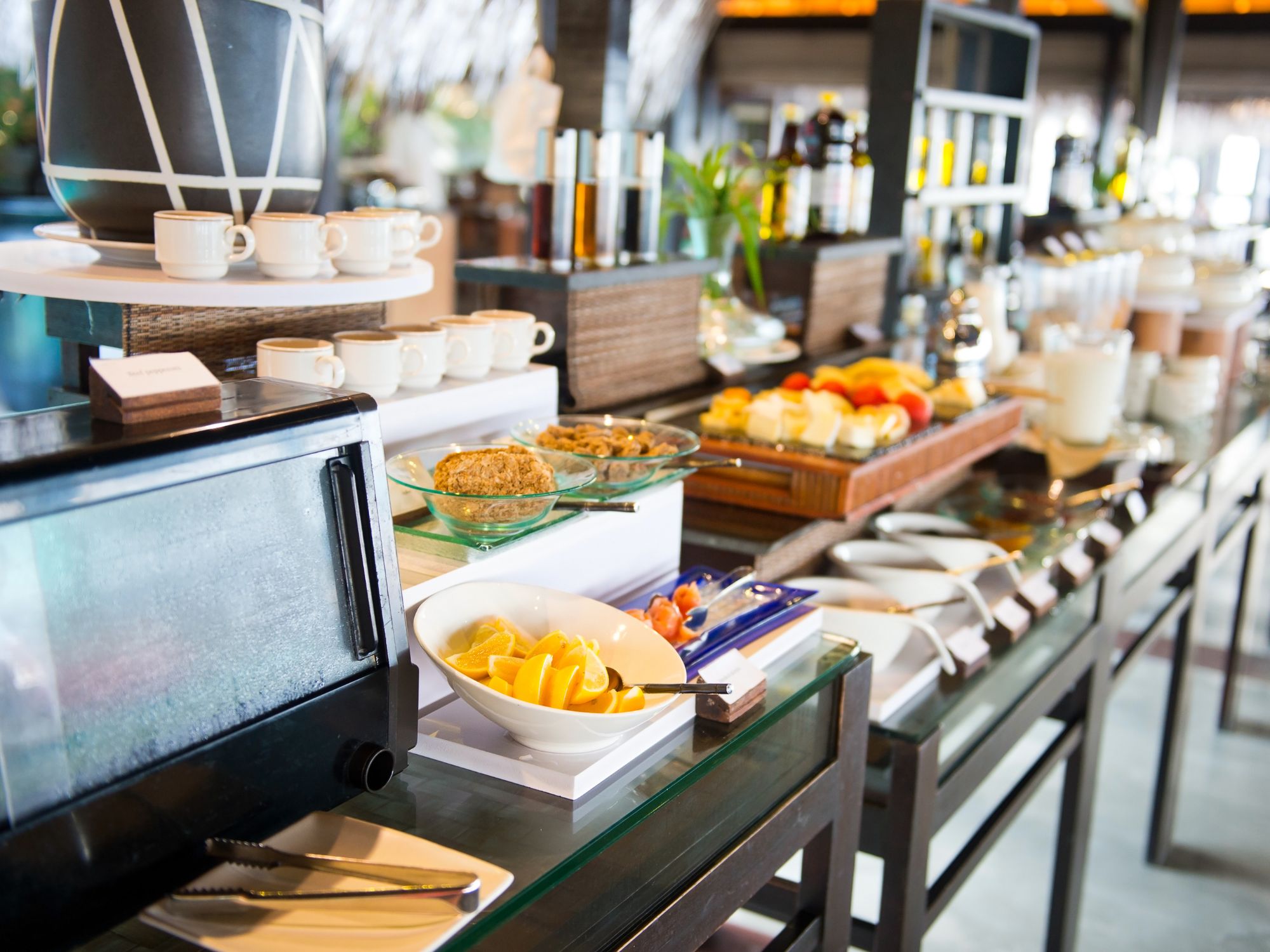 Hotel breakfast buffet with self-service food stations, beverage dispensers, and dining accessories arranged along a counter.