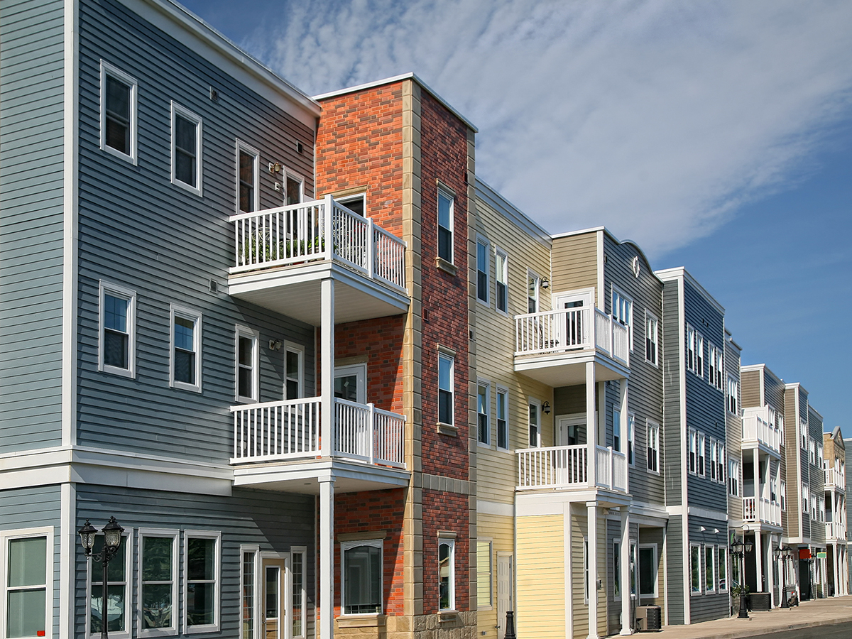 Low‑rise multifamily housing development with balconies and mixed façades along a residential street.