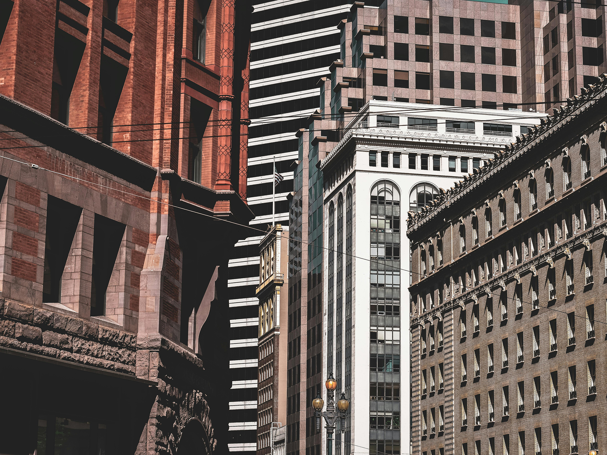 View of several tall buildings in New York City with varied architectural styles, including a red brick building with arched windows, a modern black and white striped high-rise, and a beige stone building with small windows. Additional high-rises are visible in the background, highlighting the city's dense urban landscape.