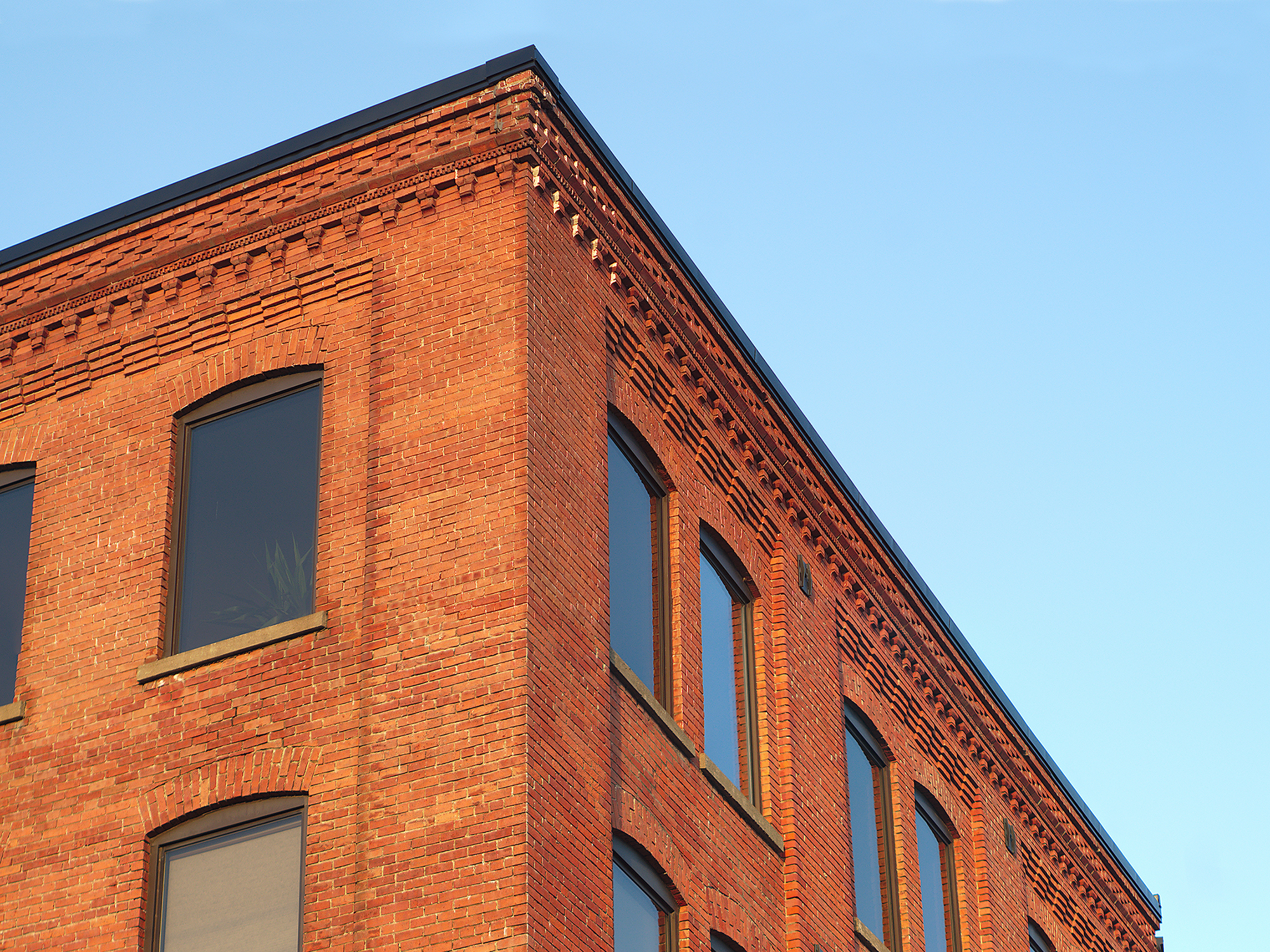 The corner of a historic red brick building with decorative brickwork along the roofline and large arched windows.