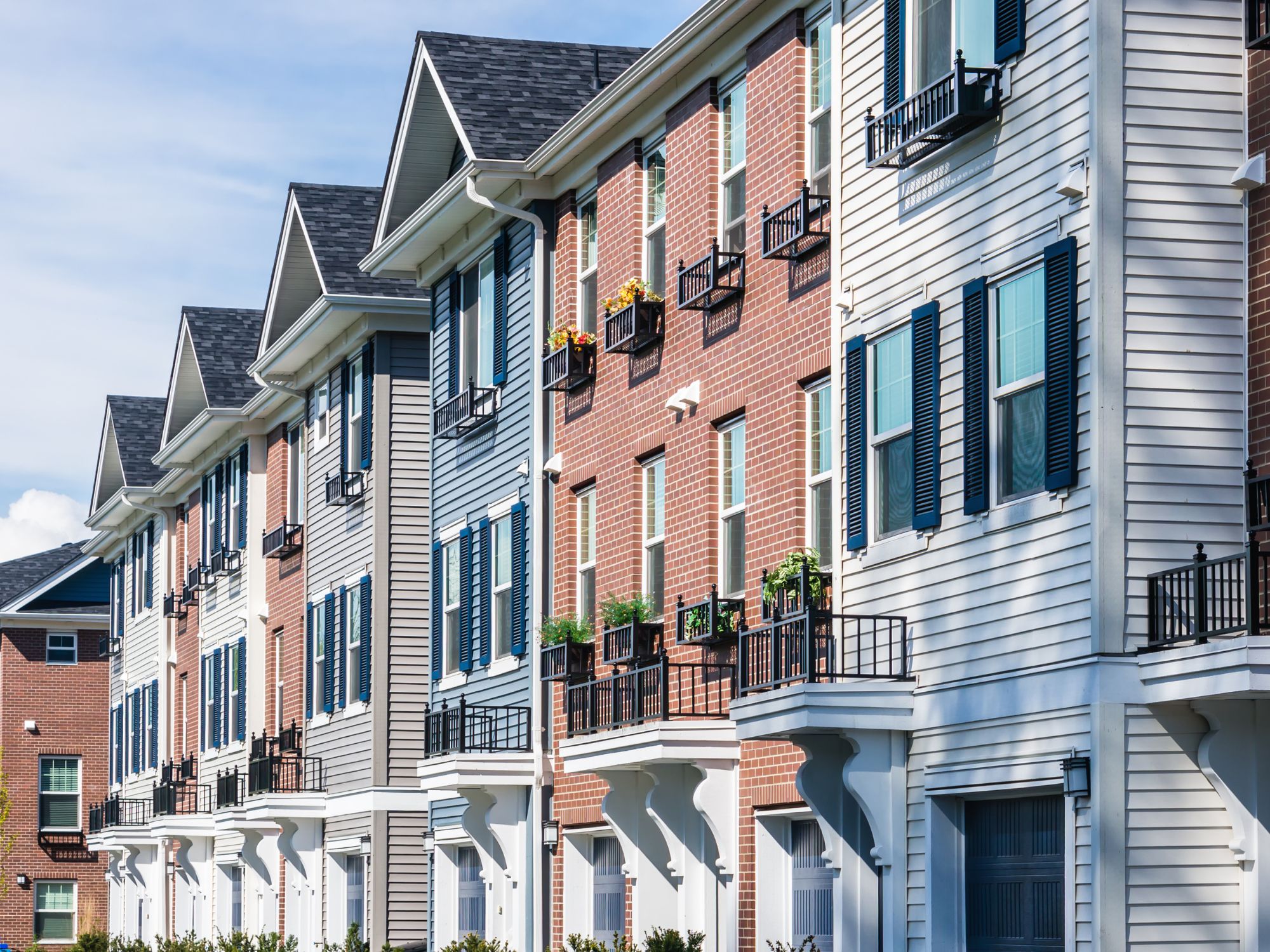 Exterior view of a multi-story multifamily residential building with brick and siding façade, balconies, and rows of windows
