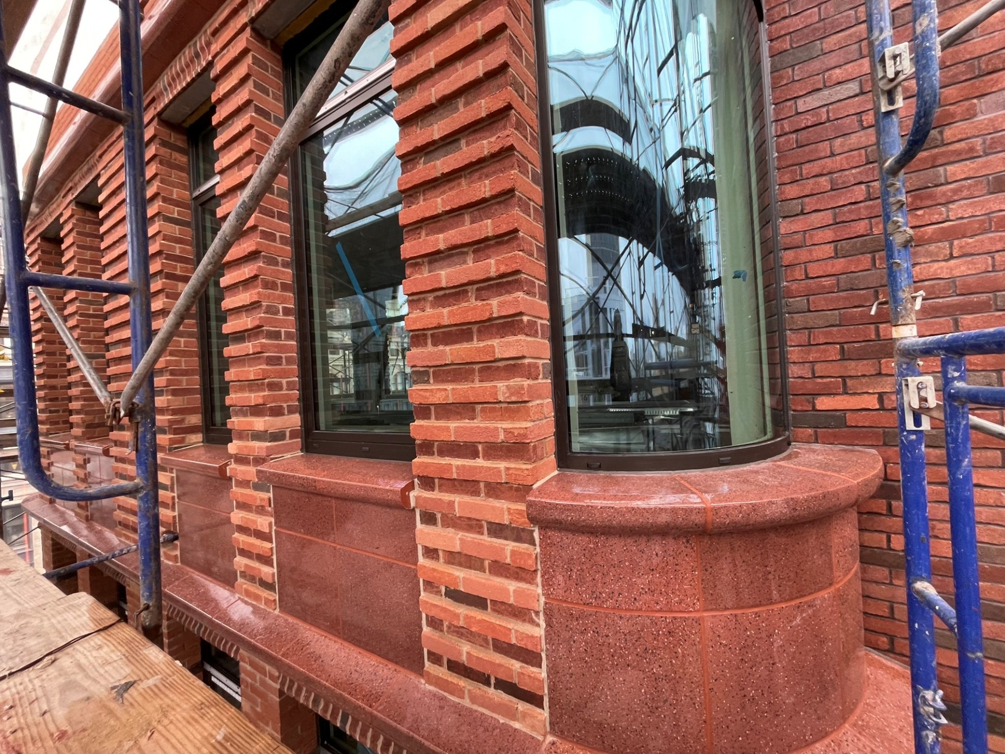 Close-up of brick masonry façade with detailed corbels, window opening, and scaffolding during construction