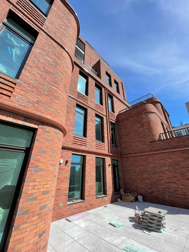 Rear courtyard with brick façade, curved corners, recessed windows, and terrace-level paving under construction