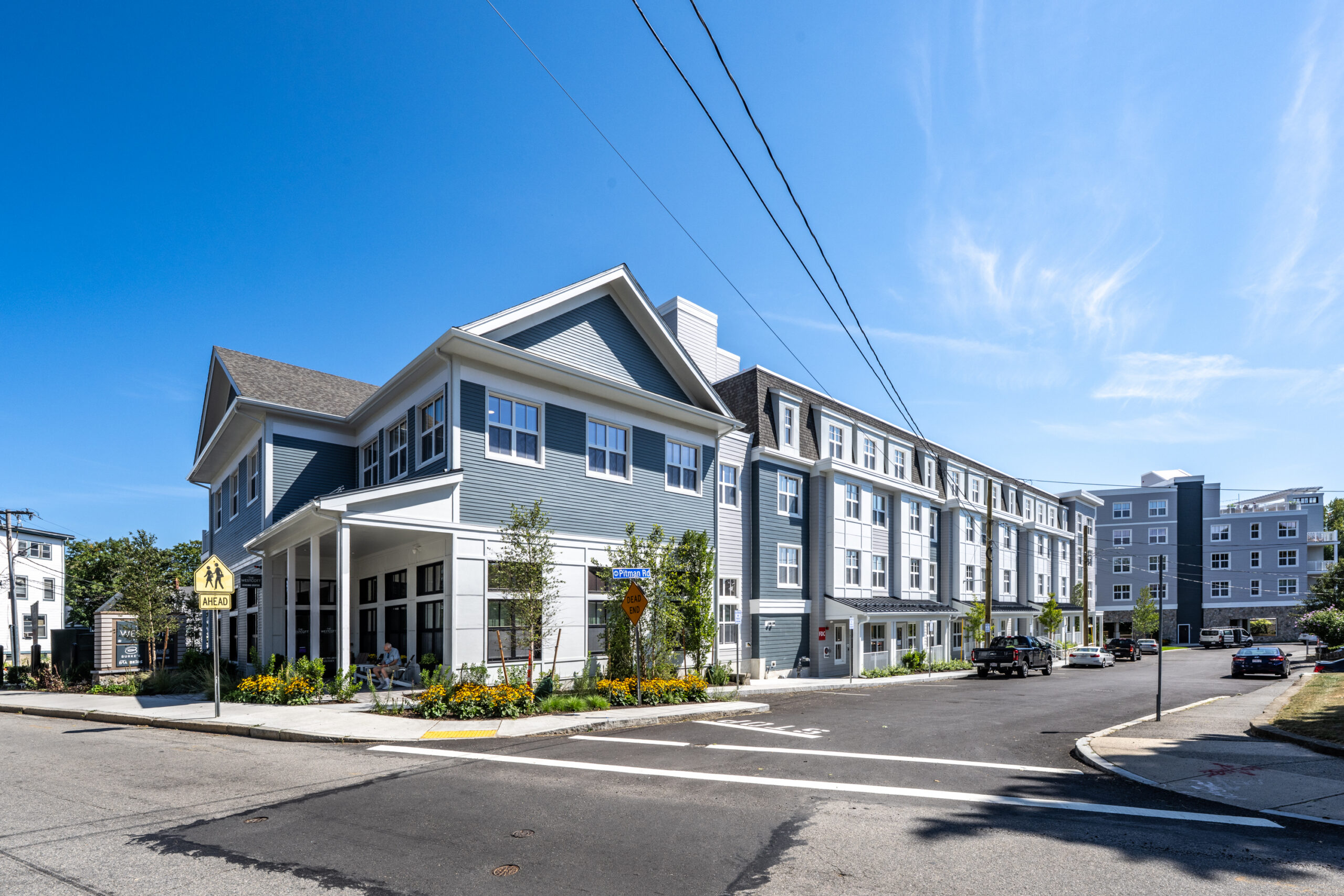 Exterior view of The Westcott, a five-story multifamily residential building in Swampscott, Massachusetts, featuring blue-gray siding, large windows, and landscaped streetscape.