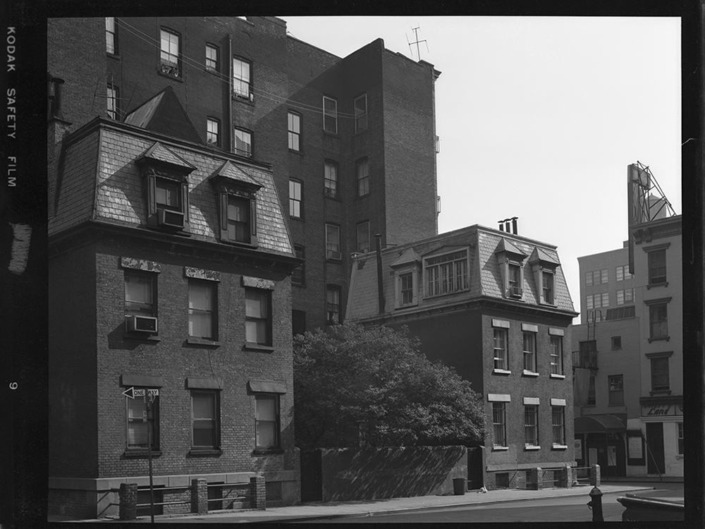 Historic black‑and‑white photograph of the Twin Sisters townhouses on Commerce Street prior to restoration, showing original mansard roofs and surrounding buildings.