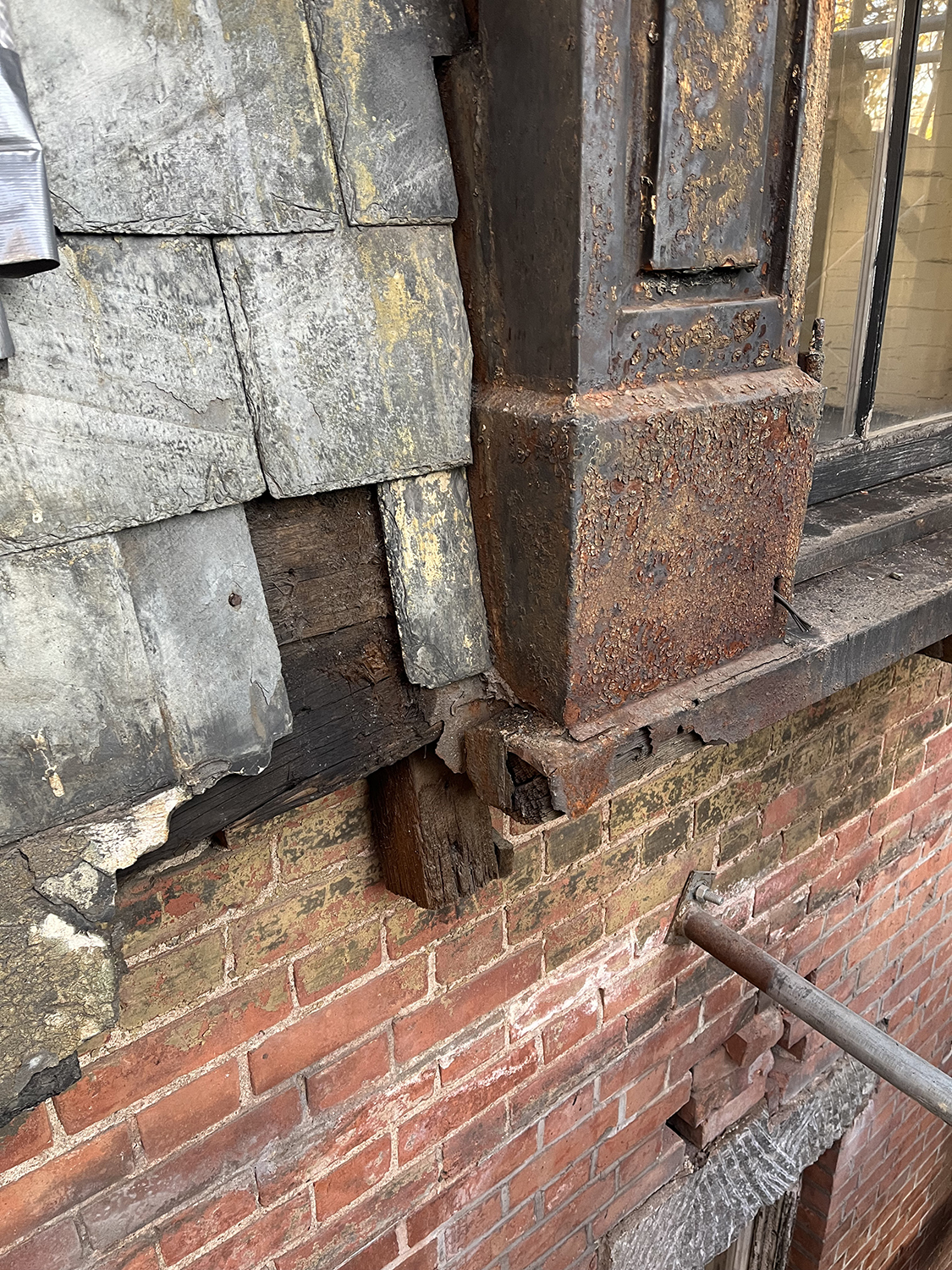 Close‑up detail of corroded metal, damaged wood framing, and masonry at the building enclosure during restoration work at the Twin Sisters.