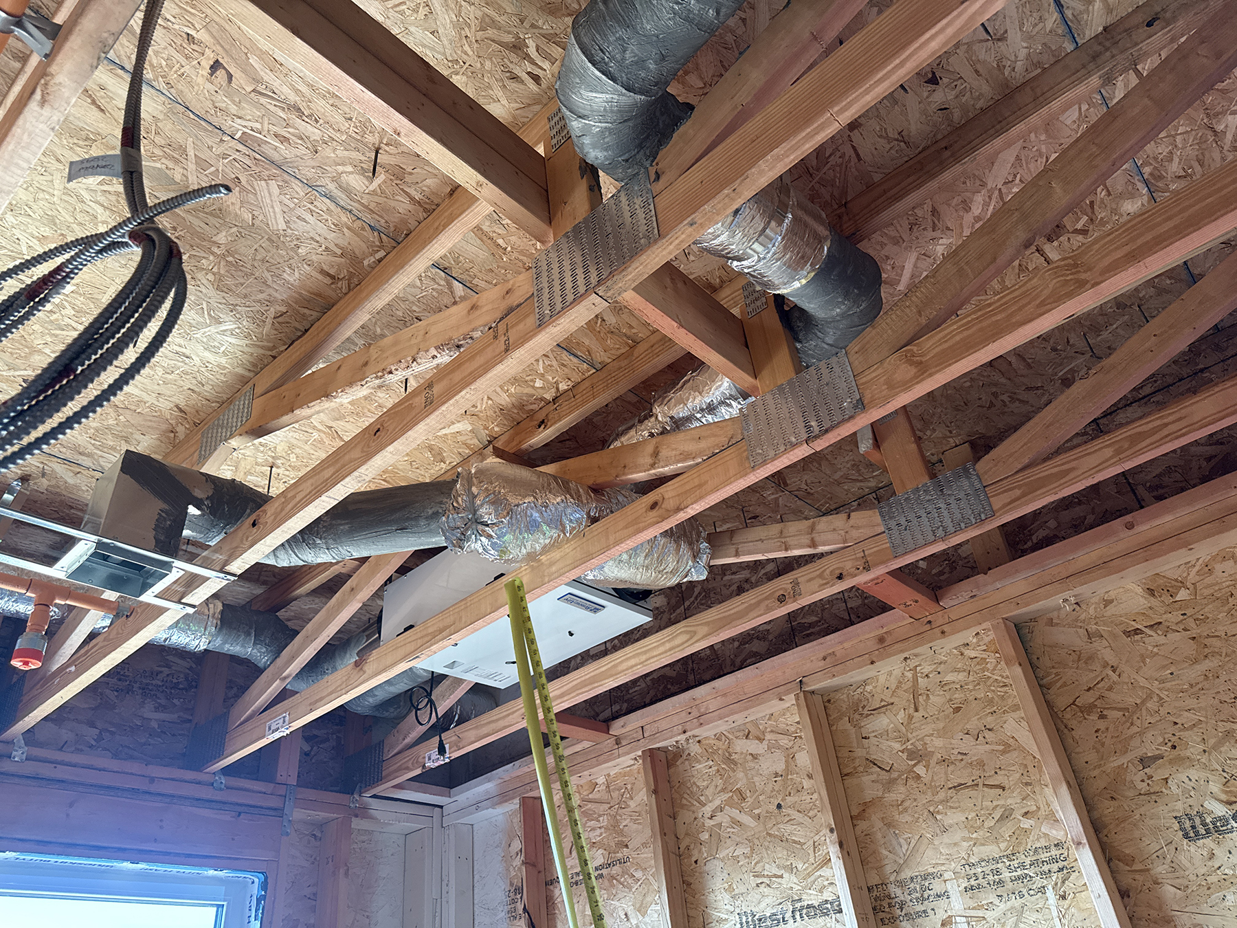Close-up of a ventilation unit connected to insulated ductwork between ceiling joists.