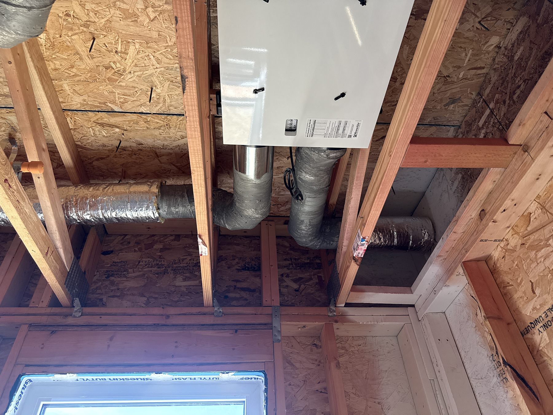 Ventilation unit with multiple insulated duct connections installed within exposed ceiling framing.