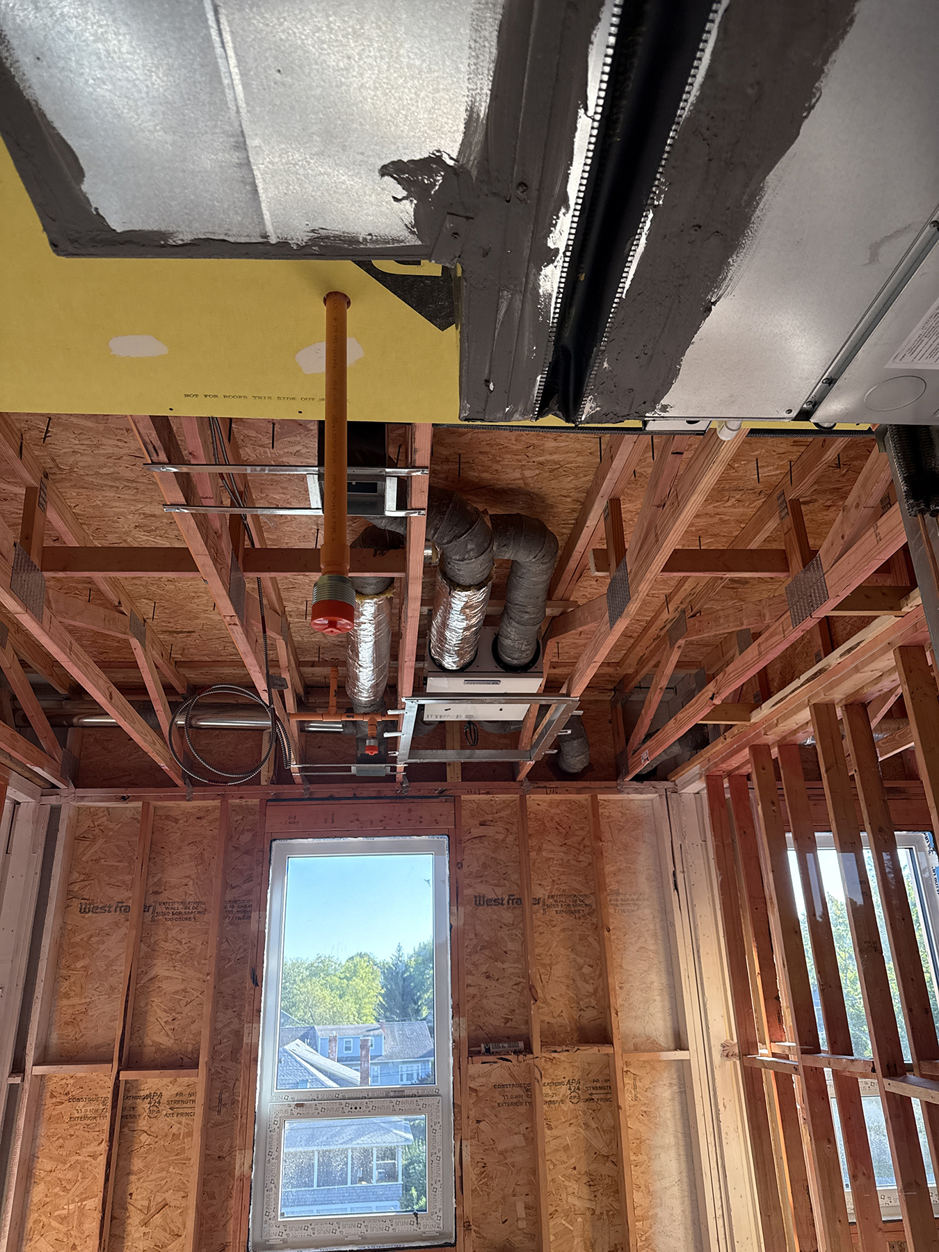 Ventilation unit and insulated ductwork installed between exposed ceiling joists in an apartment.