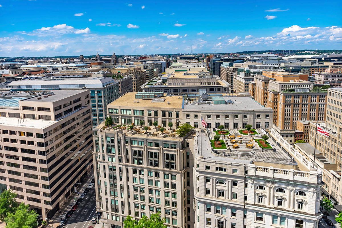 Aerial view of downtown Washington, DC showing multi‑story office buildings along Pennsylvania Avenue under a clear blue sky.